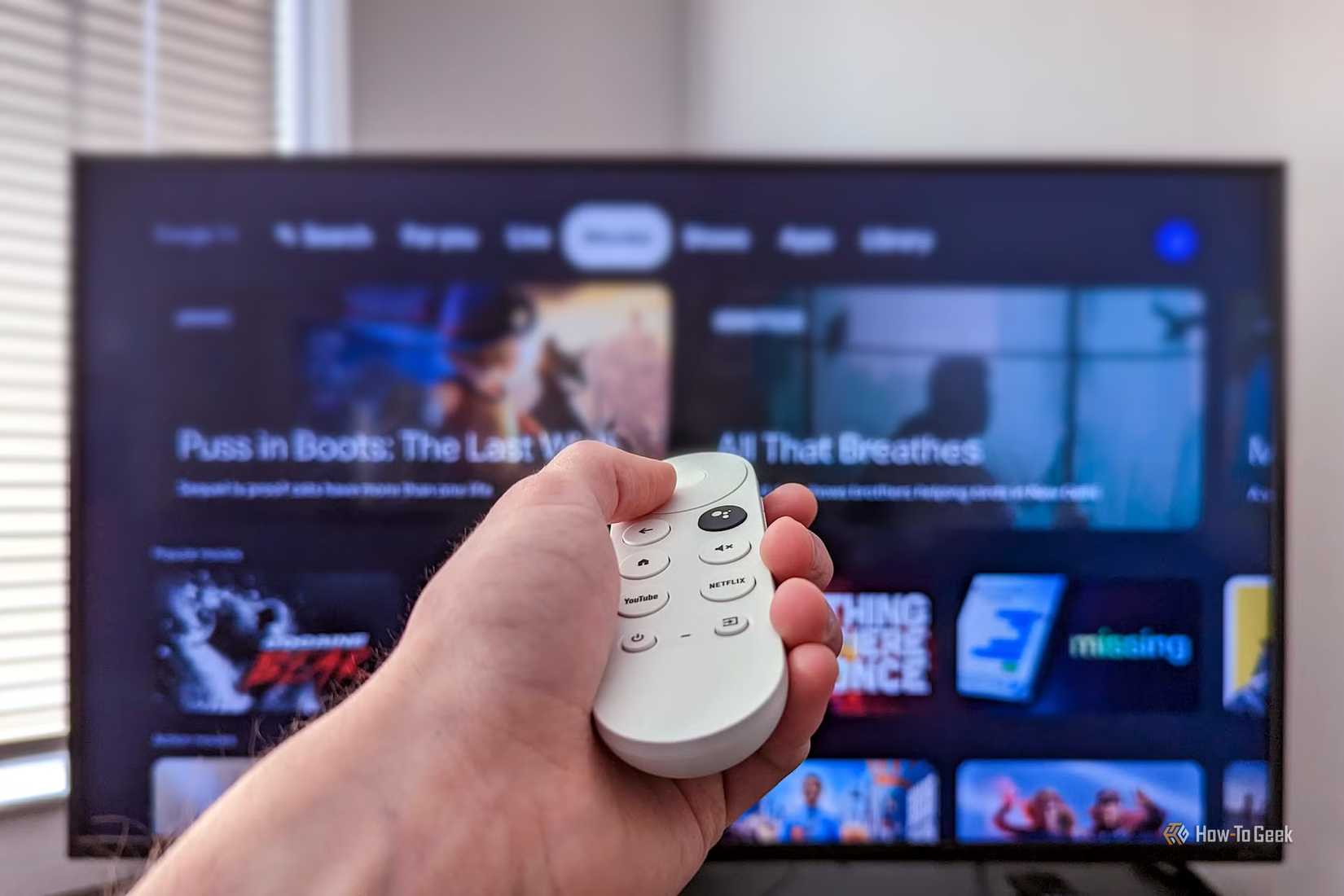 Google TV を開いた状態でテレビの前で Chromecast リモコンを持っている人。