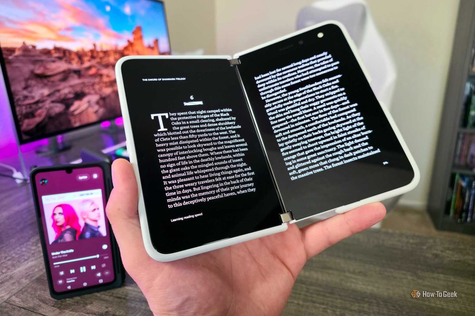 A Surface Duo open with a book displayed on both screens, and an LG V60 ThinQ with its Dual Screen Case in the background.