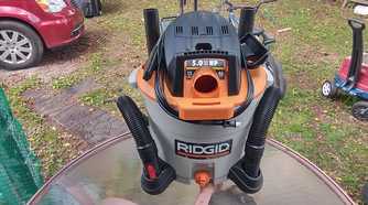 Photo of a Risgid wet and dry vac on a table with the cord wrapped and the hose sitting in the wheel's holders