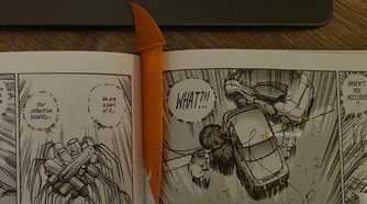 Orange shark-fin bookmark placed between the pages of an open manga book.