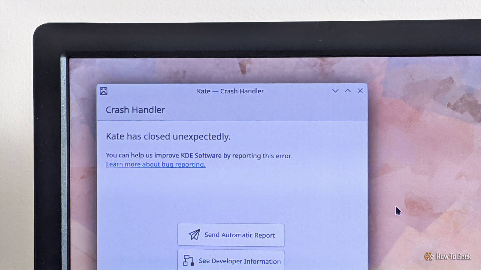 A monitor showing the KDE Crash Handler, explaining that the app Kate has crashed unexpectedly, but the user can help by reporting the error.