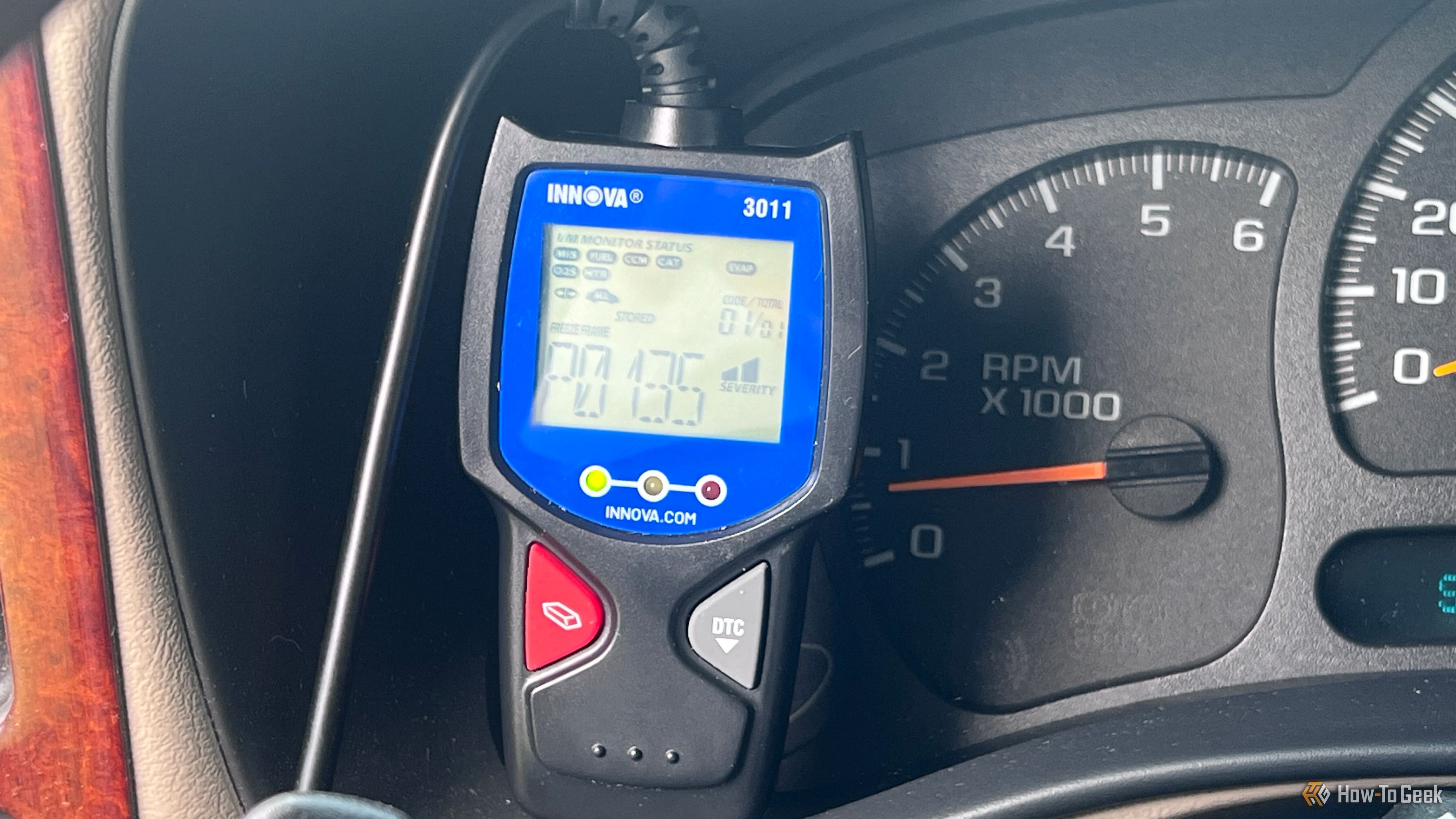 An Innova 3011 OBD-II scanner displaying a trouble code beside the vehicle's gauges.