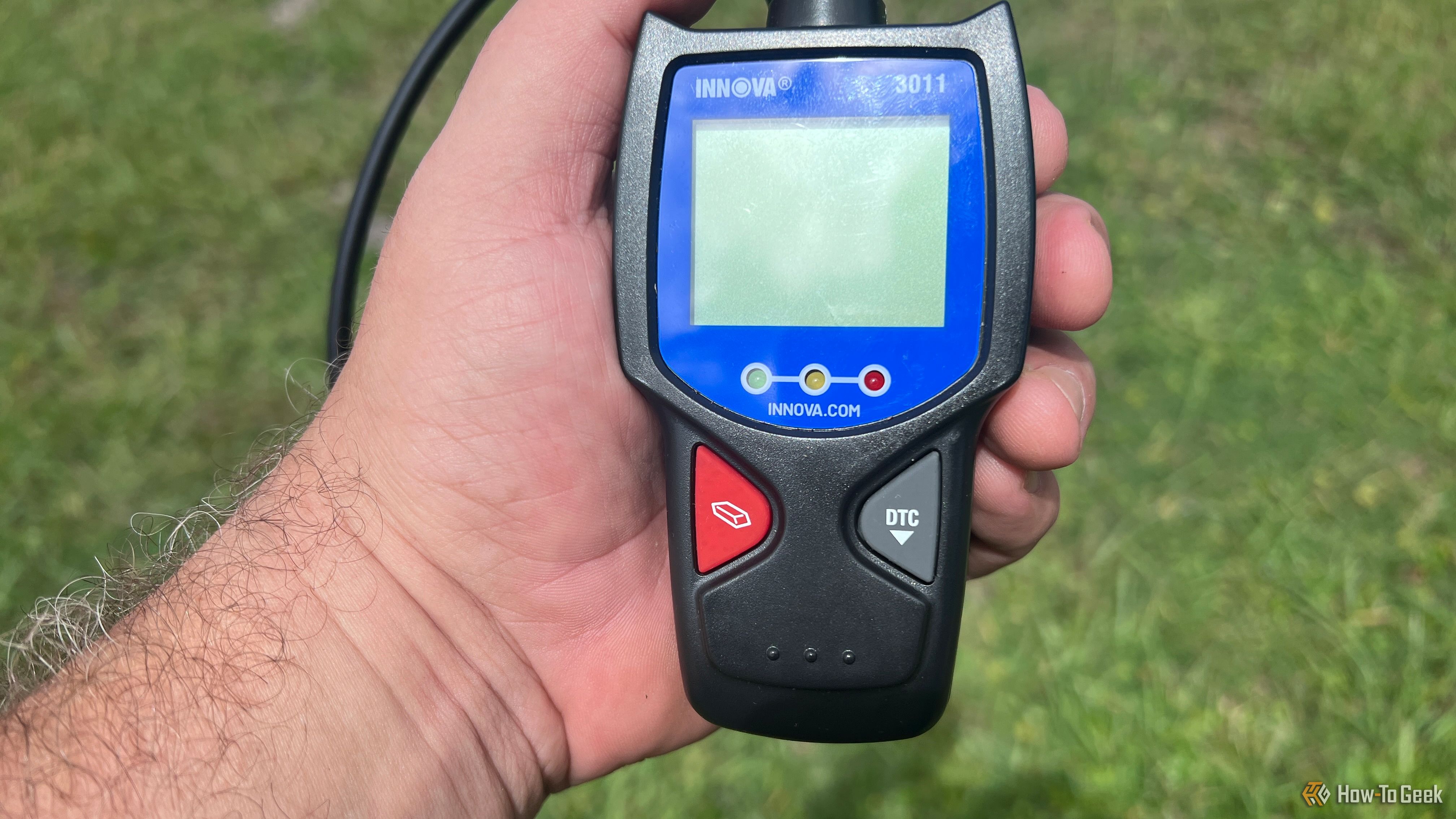 An Innova 3011 handheld OBD-II scanner held outside in the sunlight..