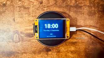 Overhead view of a Cheap Yellow Display mounted on an Echo speaker showing the time and date with a tap for smart home prompt.