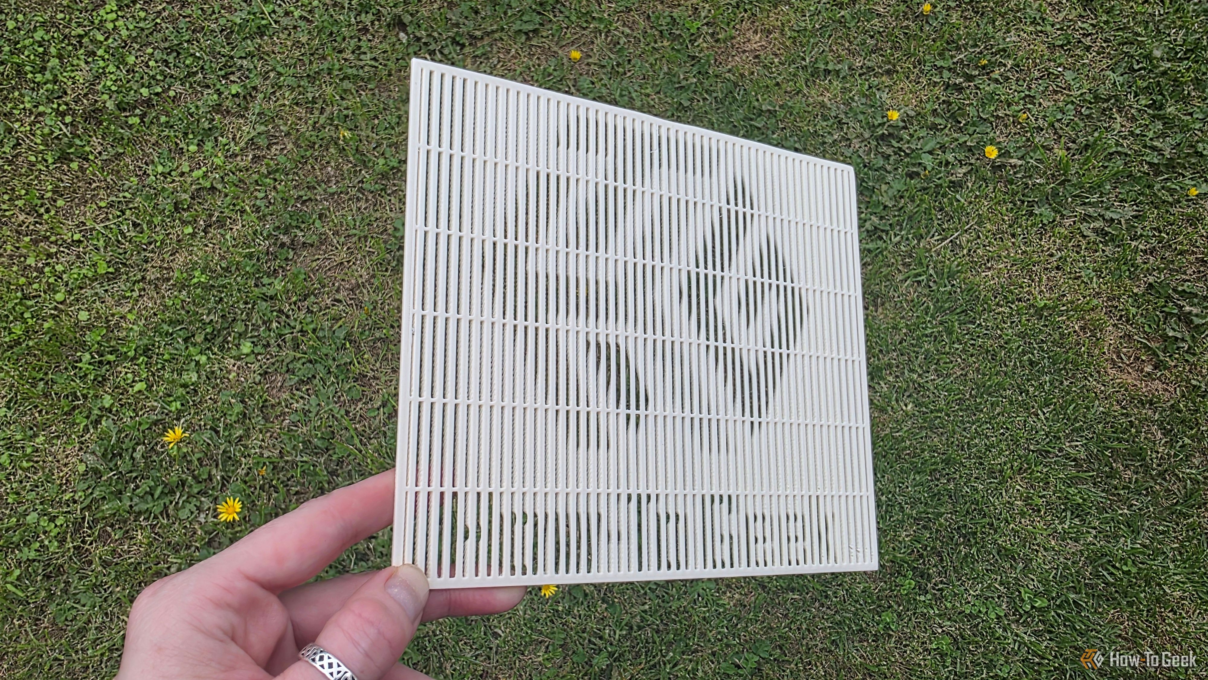 A hand holding a 3D print at a sharp angle, showing the HTG logo.