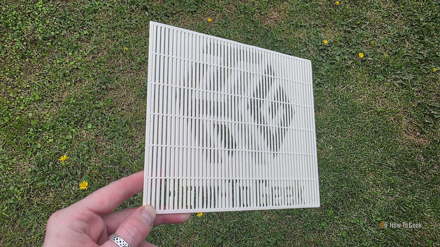 A hand holding a 3D print at a sharp angle, showing the HTG logo.