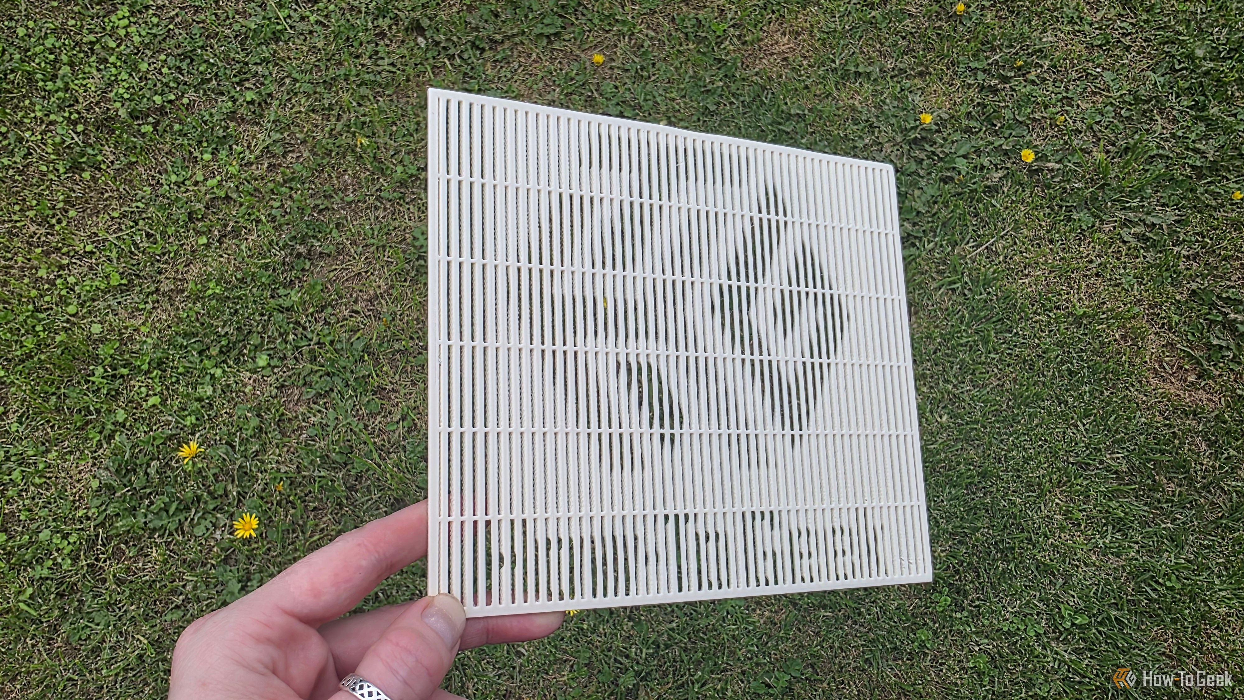 A hand holding a 3D print at a shallow angle, showing the HTG logo.