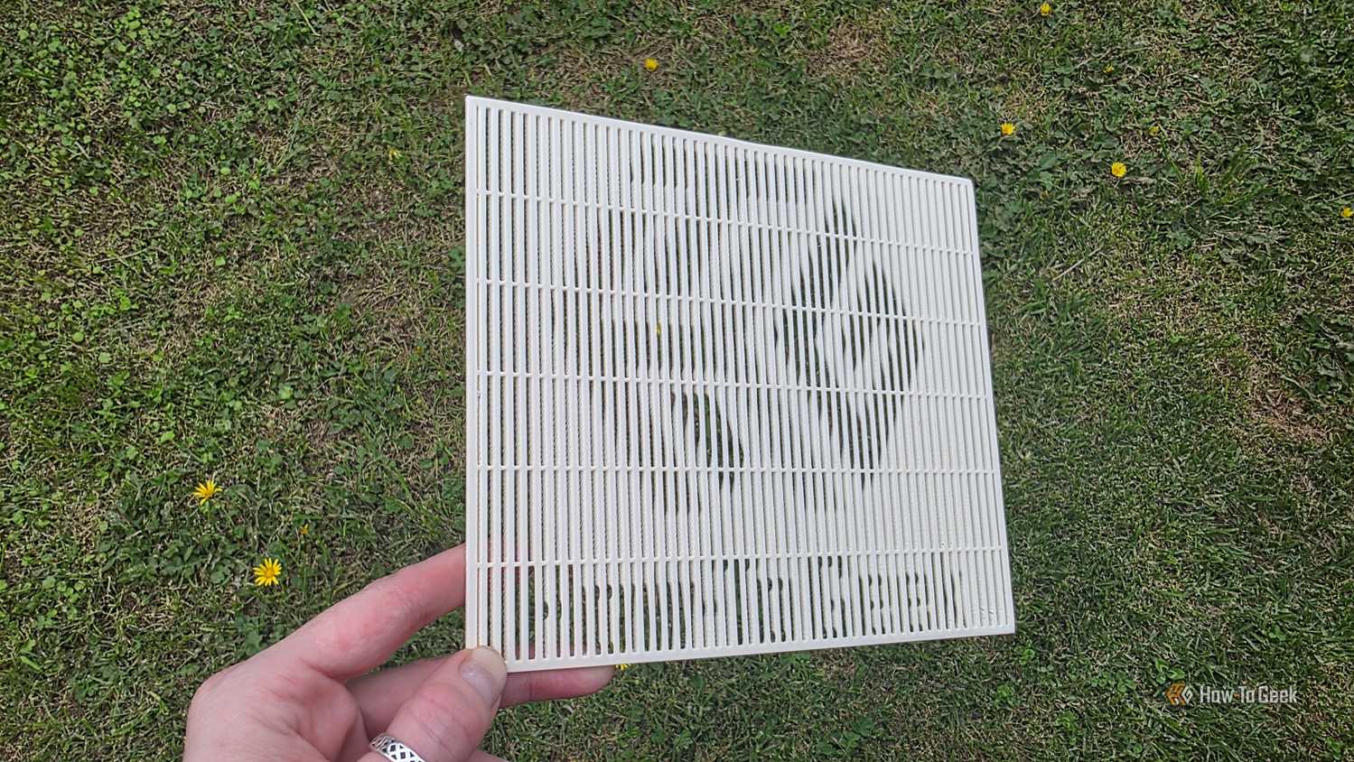 A hand holding a 3D print at a shallow angle, showing the HTG logo.