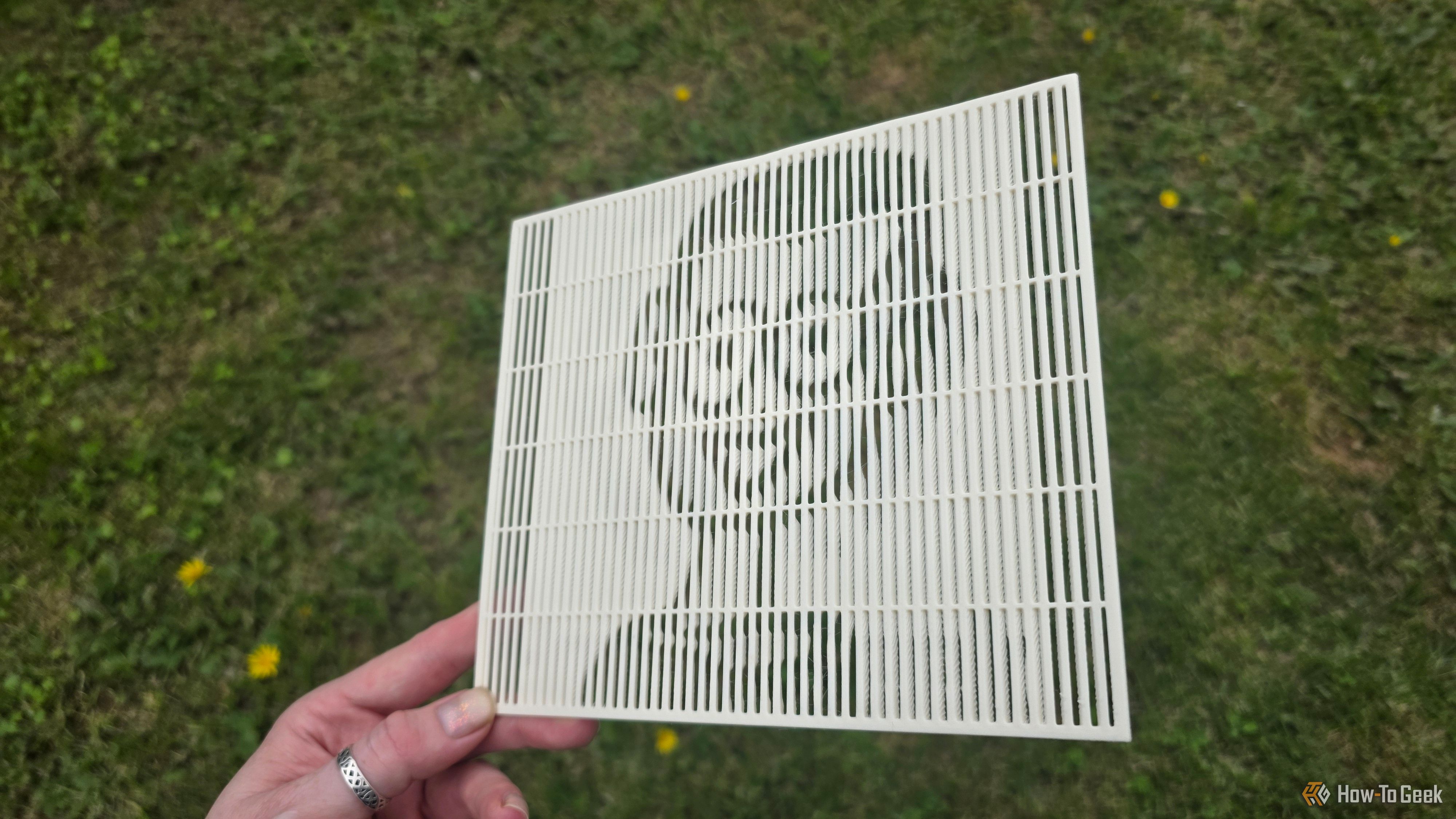 A hand holding a 3D print at a sharp angle showing the HTG mascot's face.