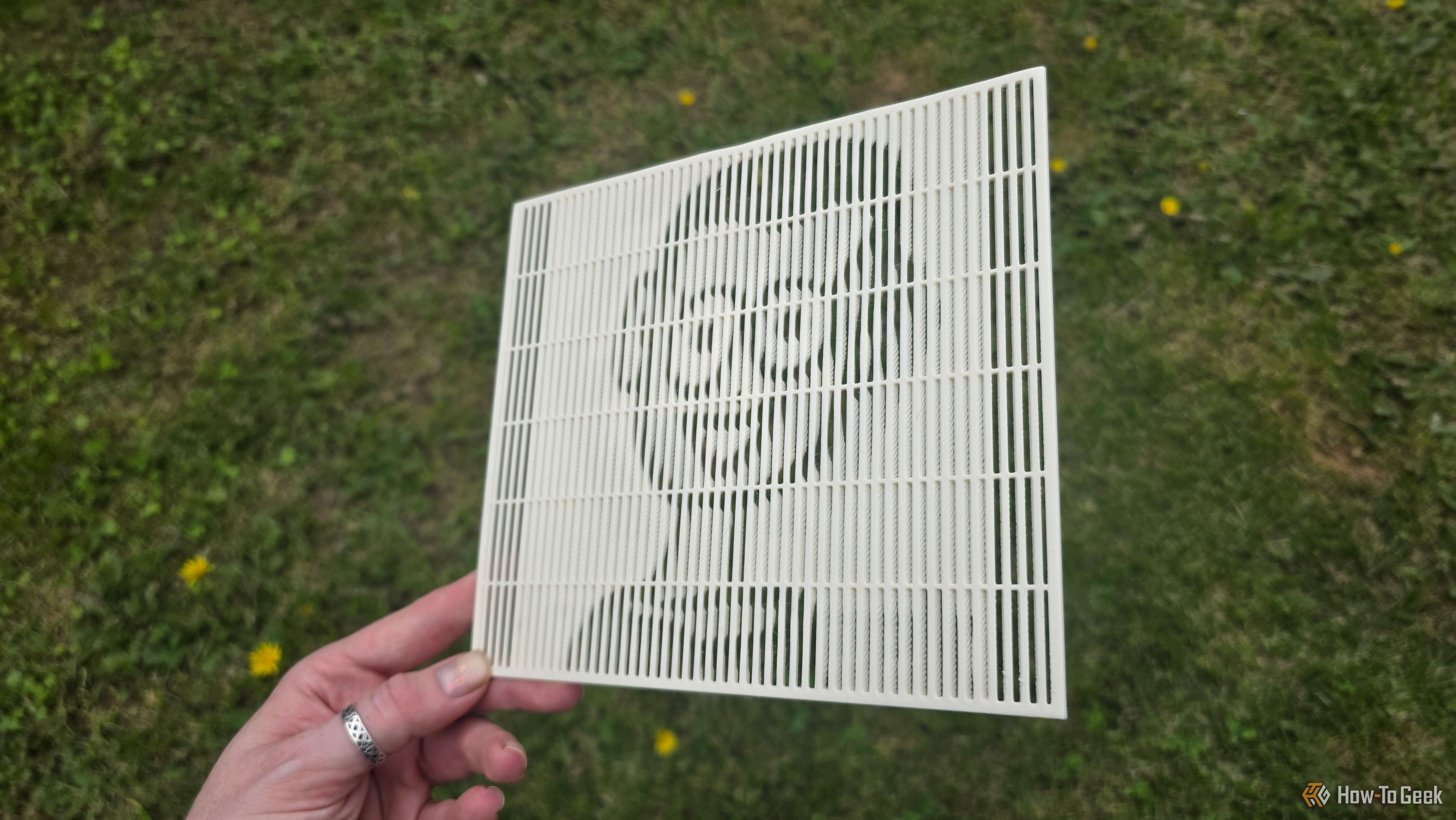 A hand holding a 3D print at a sharp angle showing the HTG mascot's face.