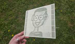 A hand holding a 3D print at a sharp angle showing the HTG mascot's face.