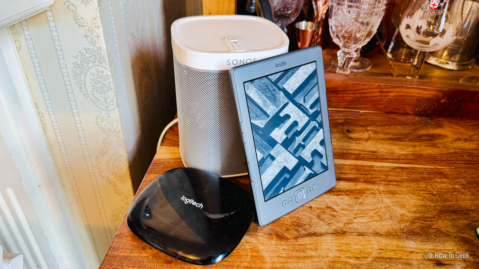 A Logitech Harmony Hub, a Kindle 4, and a Sonos Play 1 on a cabinet.