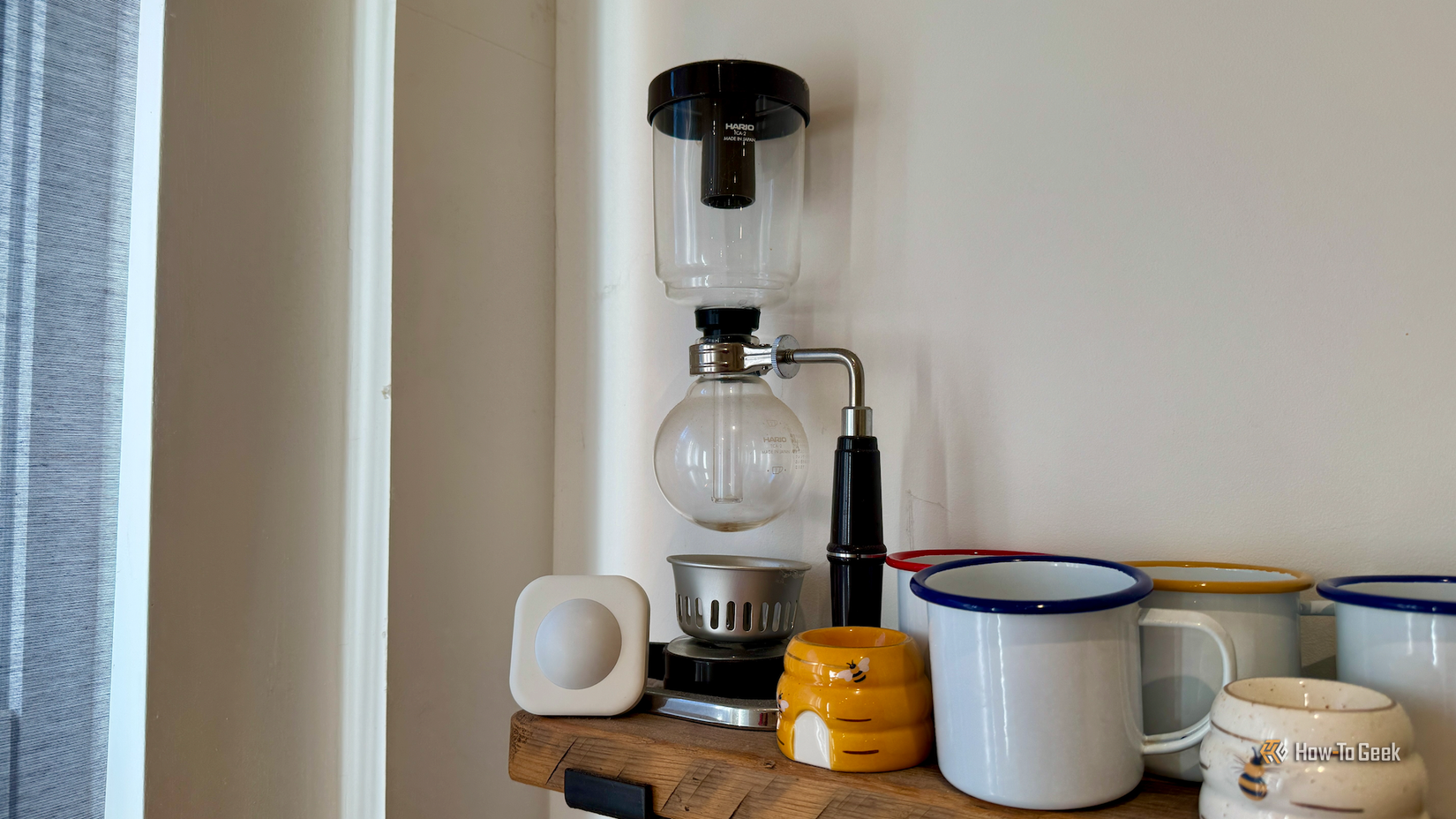 A motion sensor on a kitchen shelf next to a coffee siphon.