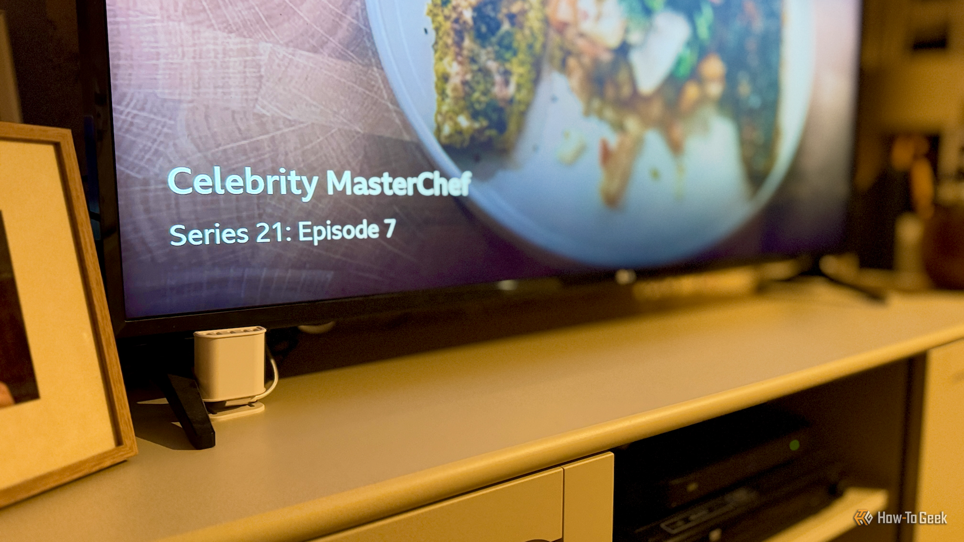 An Everything Presence Lite presence sensor in front of a TV showing Celebrity Masterchef with the show paused.