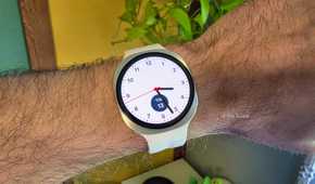 Samsung Galaxy smartwatch with a white strap and an analogue watch face displaying the time, worn on a person's wrist.
