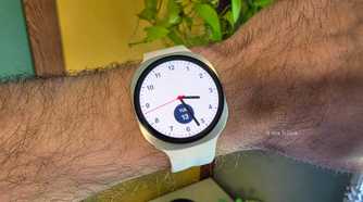Samsung Galaxy smartwatch with a white strap and an analogue watch face displaying the time, worn on a person's wrist.