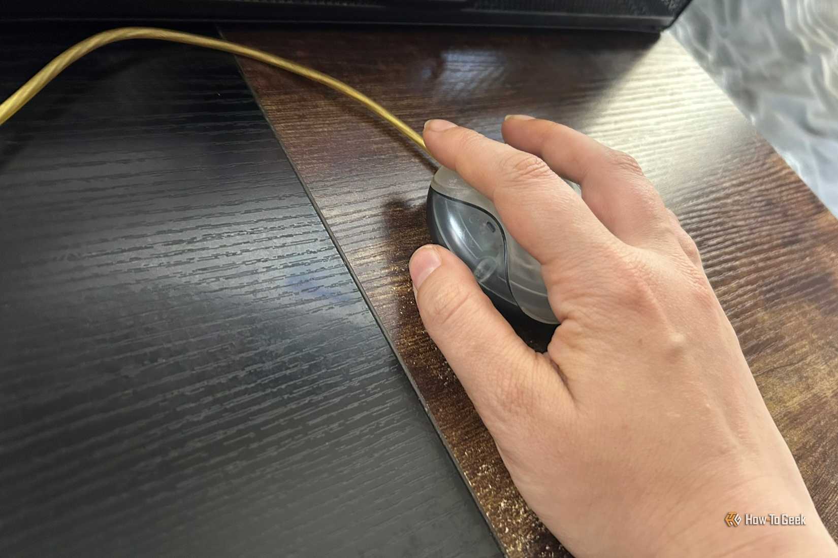A hand rests on a classic Apple USB hockey puck mouse on a wooden surface.