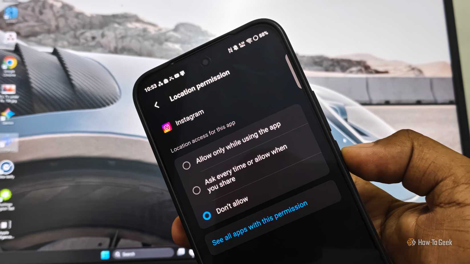 Android phone displaying Instagram’s location permission settings with “Don’t allow” selected, held in front of a desktop monitor.