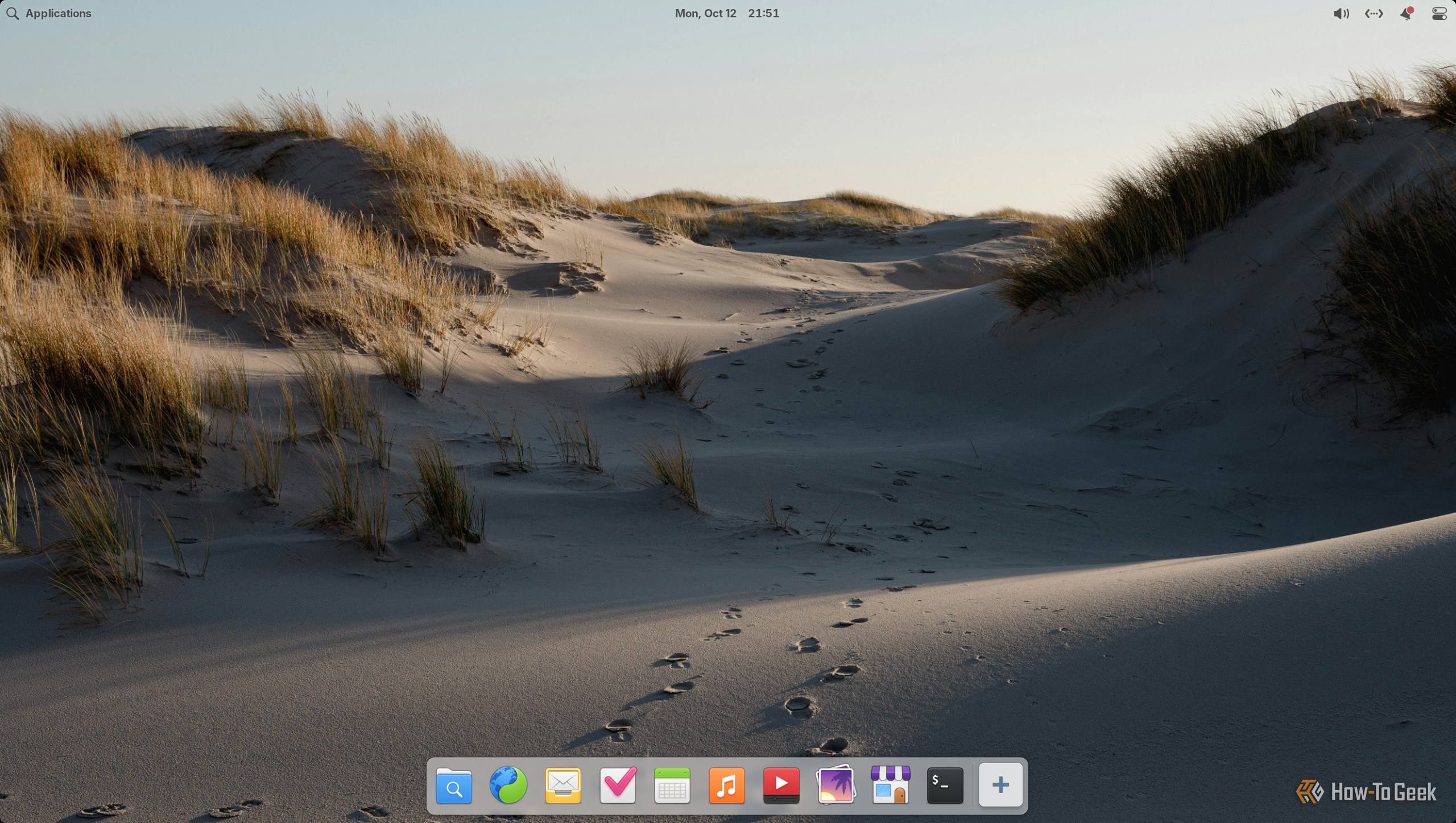 Pantheon desktop on elementary OS with the top panel and macOS-style bottom dock over a sand dune wallpaper.