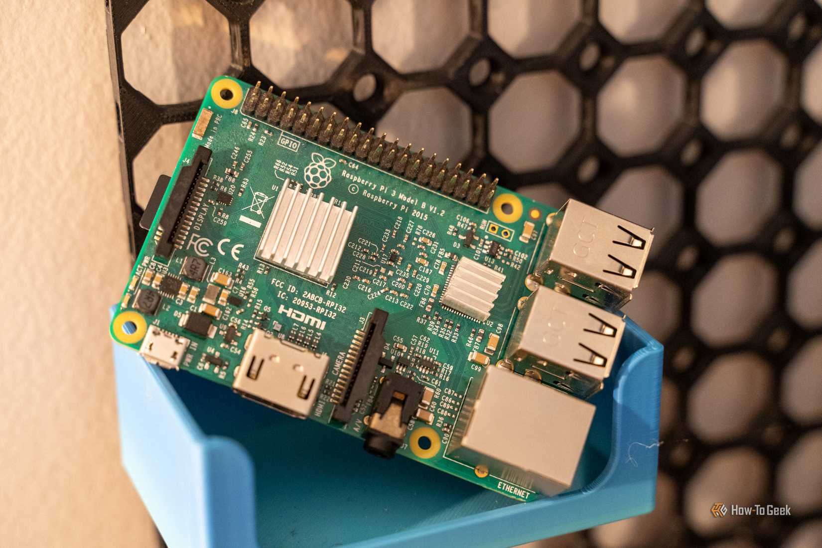 Raspberry Pi 3 Model B resting at an angle in a blue storage bin on a black wall organizer.