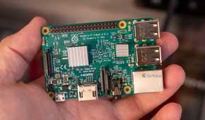 Raspberry Pi 3 Model B held in a hand, showing two silver heatsinks and its connectors.