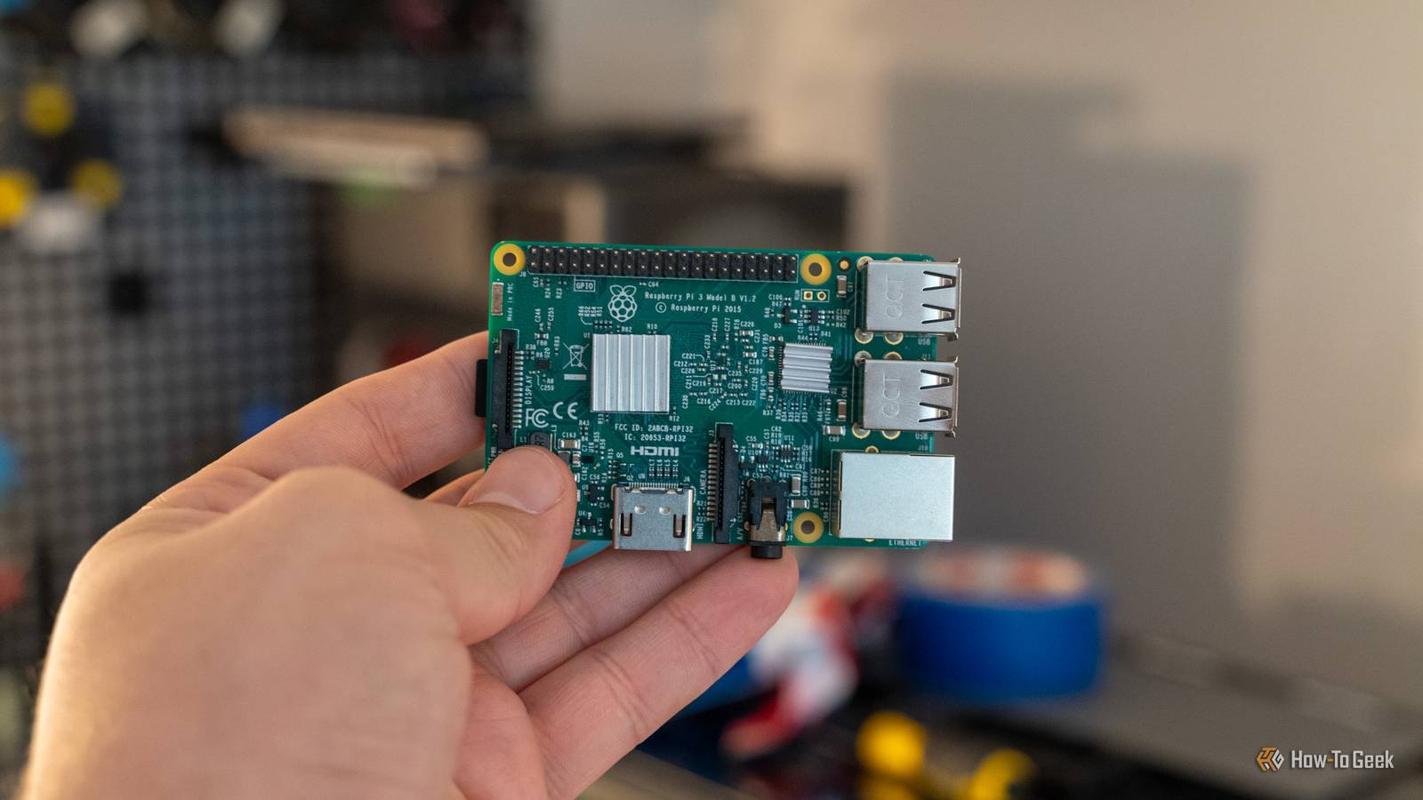 Raspberry Pi 3 Model B held up in front of a blurred workshop background.