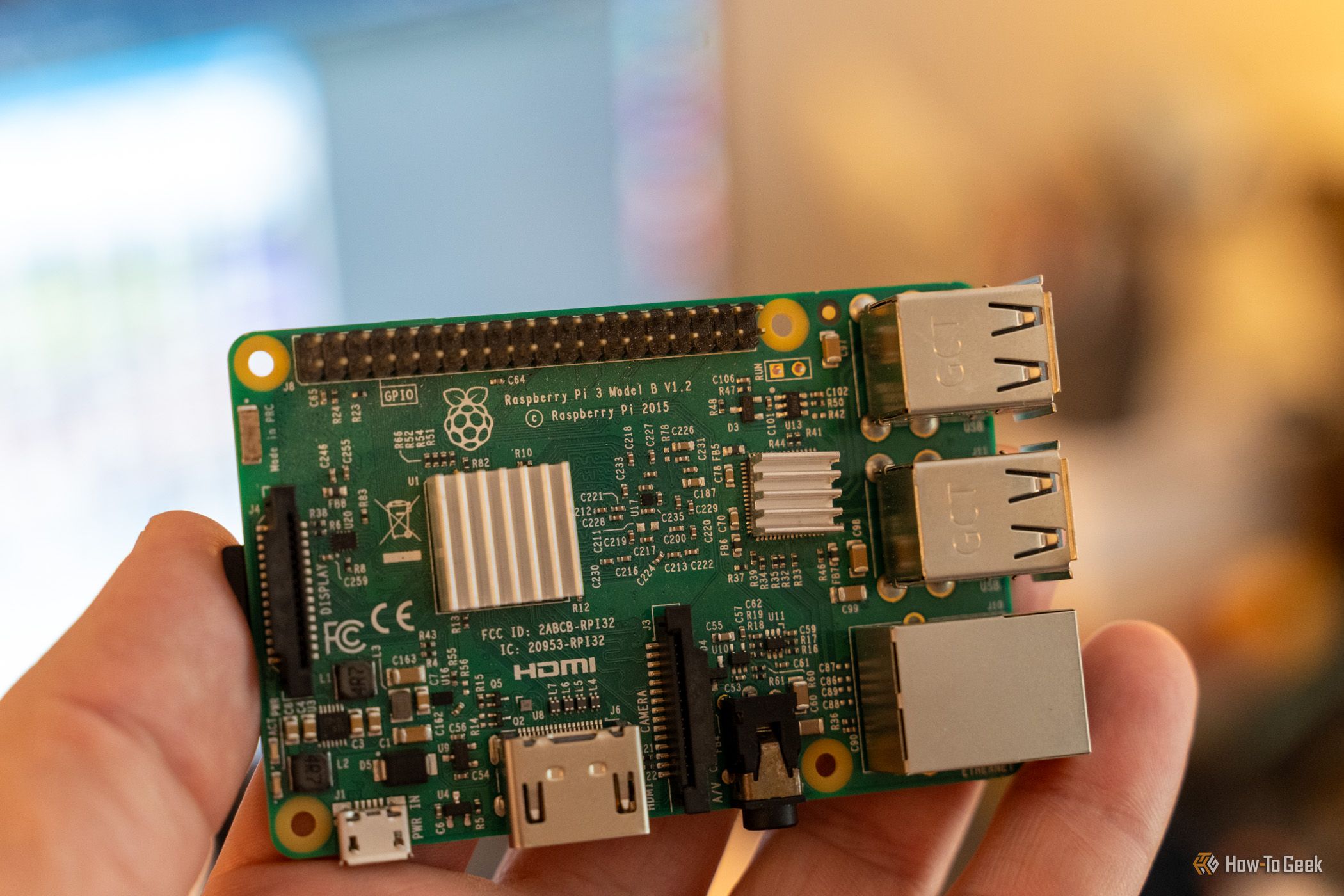 Close-up of a Raspberry Pi 3 Model B held in a hand, showing the V1.2 board label, GPIO header, and heatsinks.