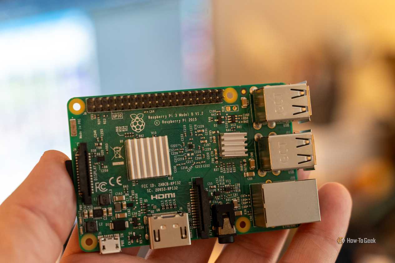 Close-up of a Raspberry Pi 3 Model B held in a hand, showing the V1.2 board label, GPIO header, and heatsinks.
