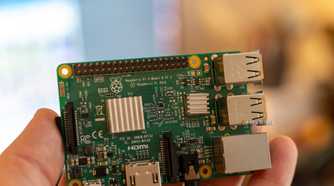Close-up of a Raspberry Pi 3 Model B held in a hand, showing the V1.2 board label, GPIO header, and heatsinks.
