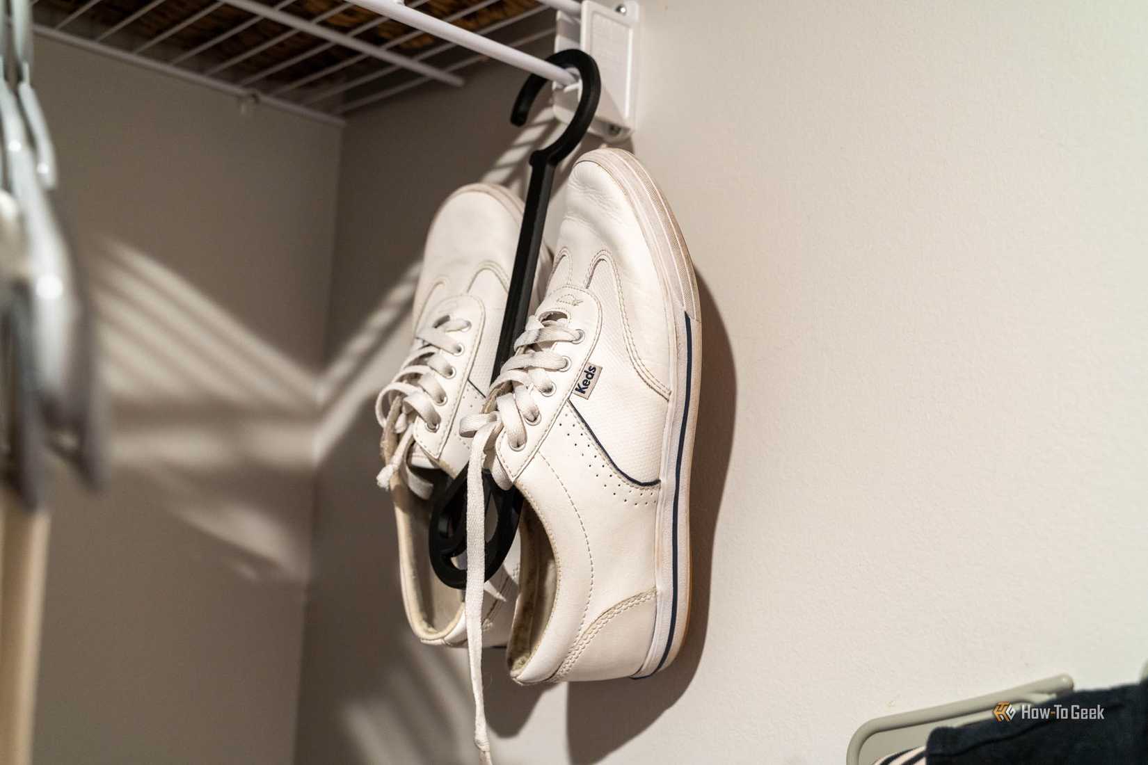Side view of white Keds sneakers held by their heels on a black 3D-printed shoe hanger.