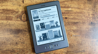 The Bookshelf home screen on a Kindle 4 showing the current book and bookshelves with other books and potted plants on the shelves.