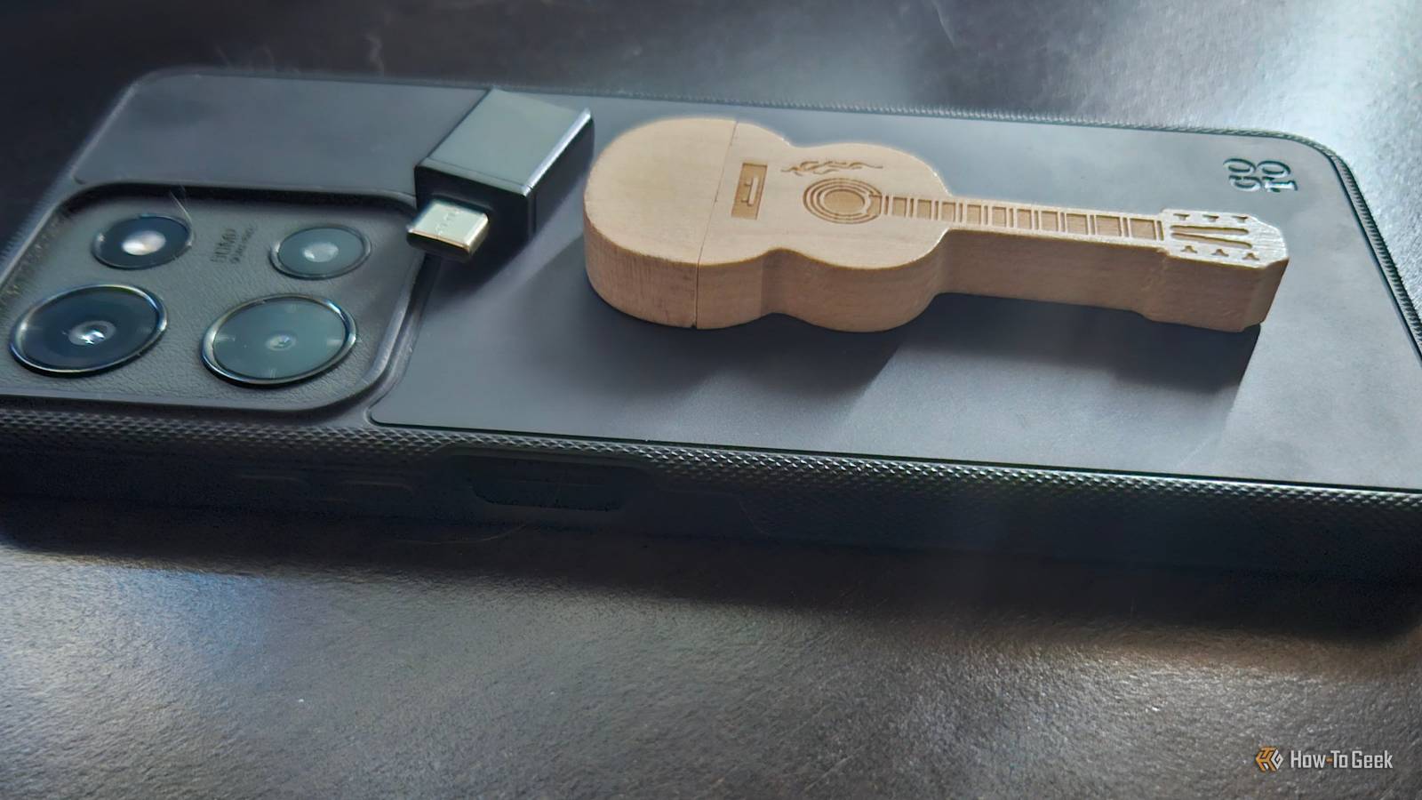 A phone with a USB adapter and a guitar-shaped wooden USB drive on top of it.
