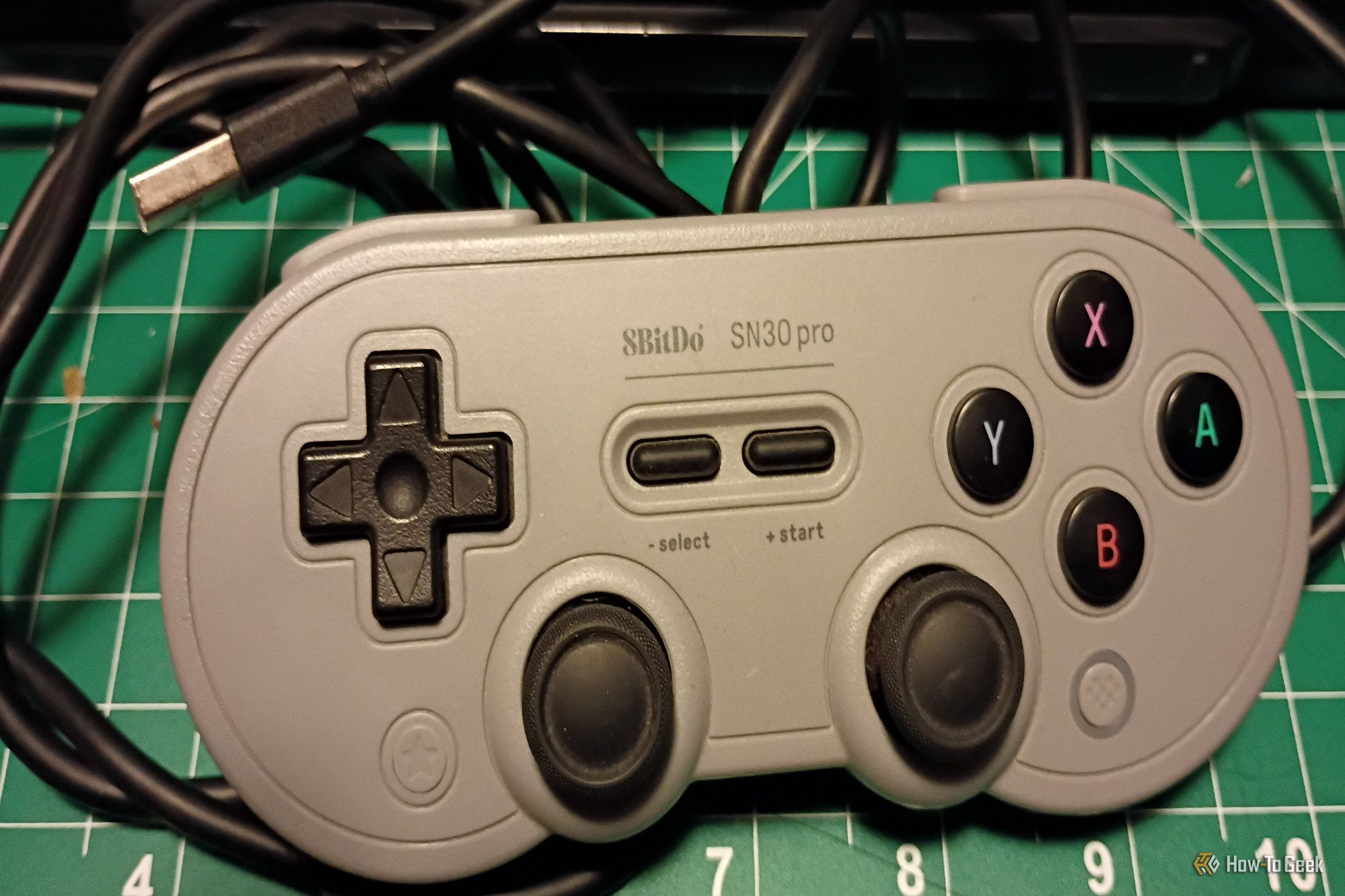 A gray USB 8bitDo controller on a green mat.
