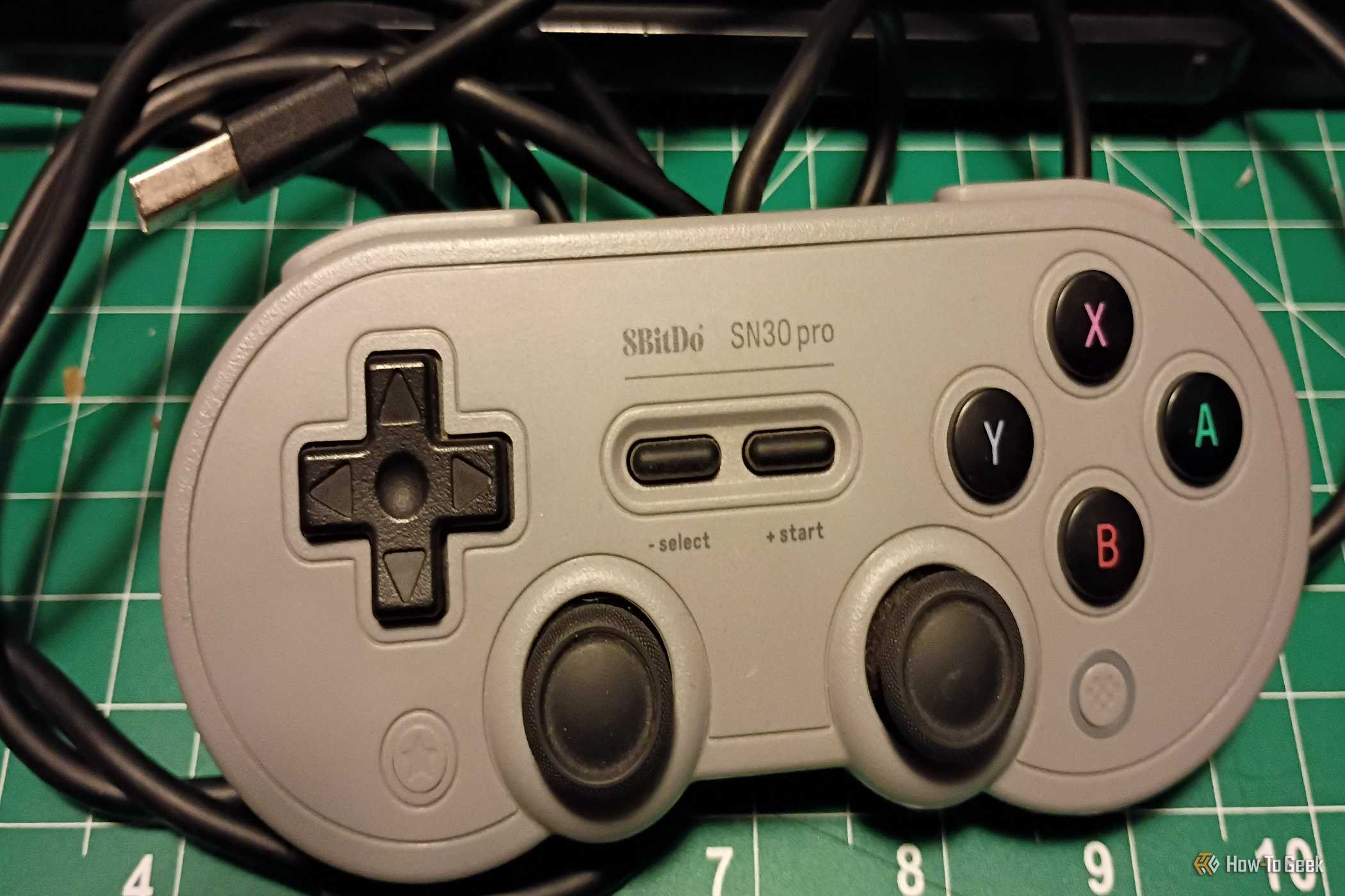 A gray USB 8bitDo controller on a green mat.