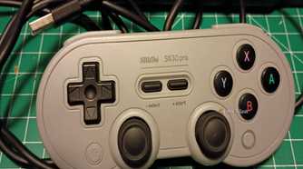 A gray USB 8bitDo controller on a green mat.