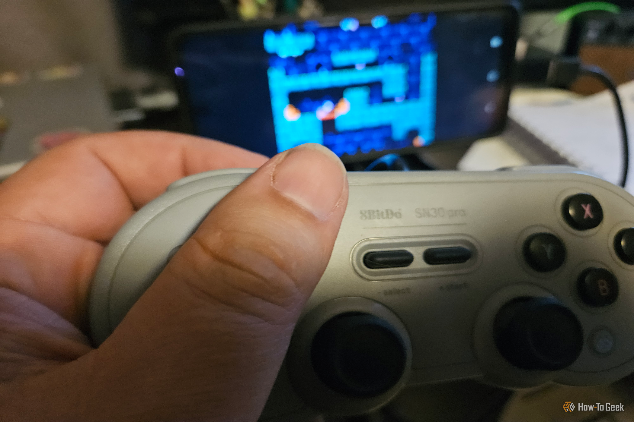 A hand holds a gray 8BitDo controller while playing a game on an Android screen.