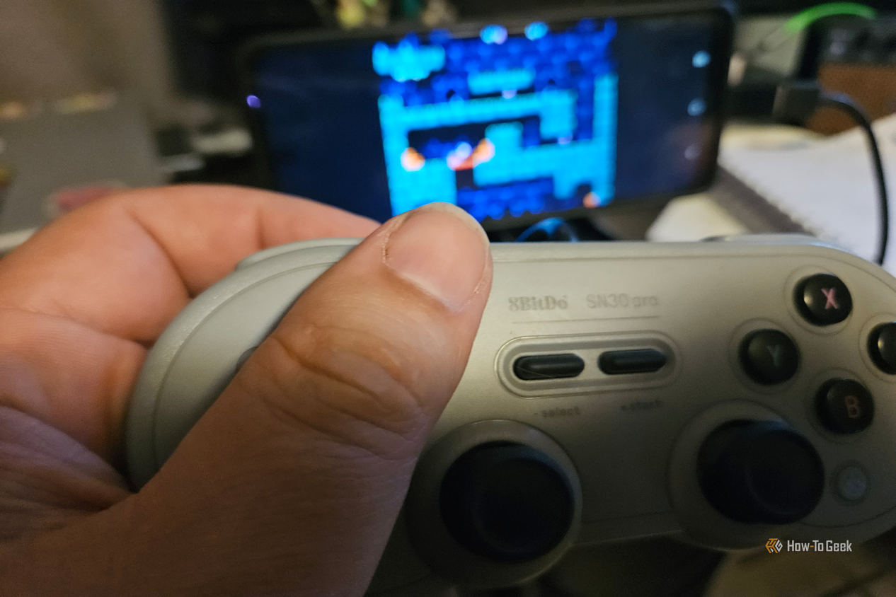 A hand holds a gray 8BitDo controller while playing a game on an Android screen.