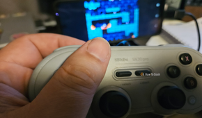 A hand holds a gray 8BitDo controller while playing a game on an Android screen.