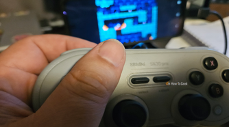A hand holds a gray 8BitDo controller while playing a game on an Android screen.