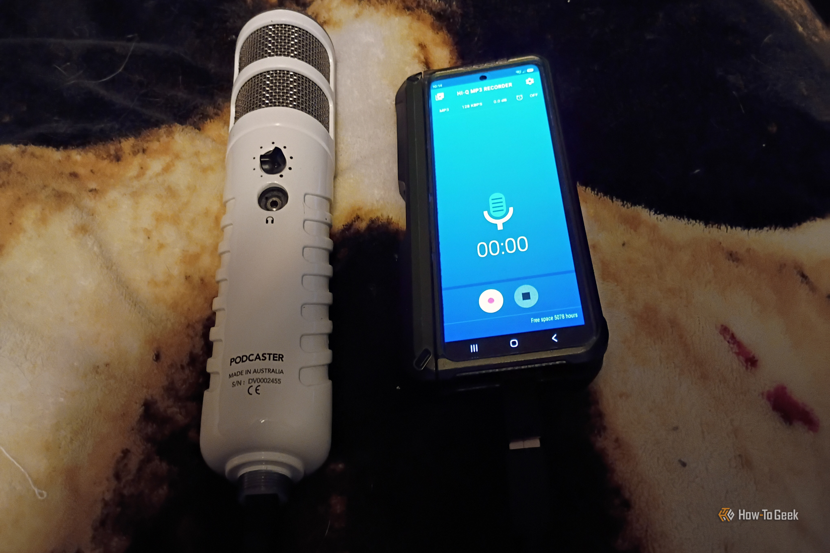 A white Rode Podcaster mic sits next to a phone with a blue recording display on the screen.