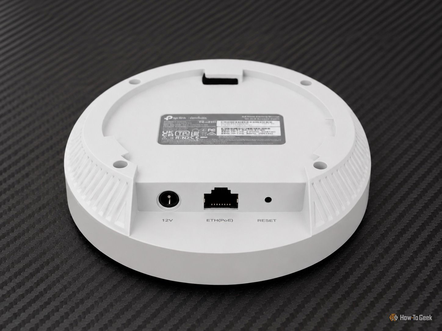 White TP-Link Omada access point shown from the underside, with 12V, Ethernet, PoE, and reset ports visible.
